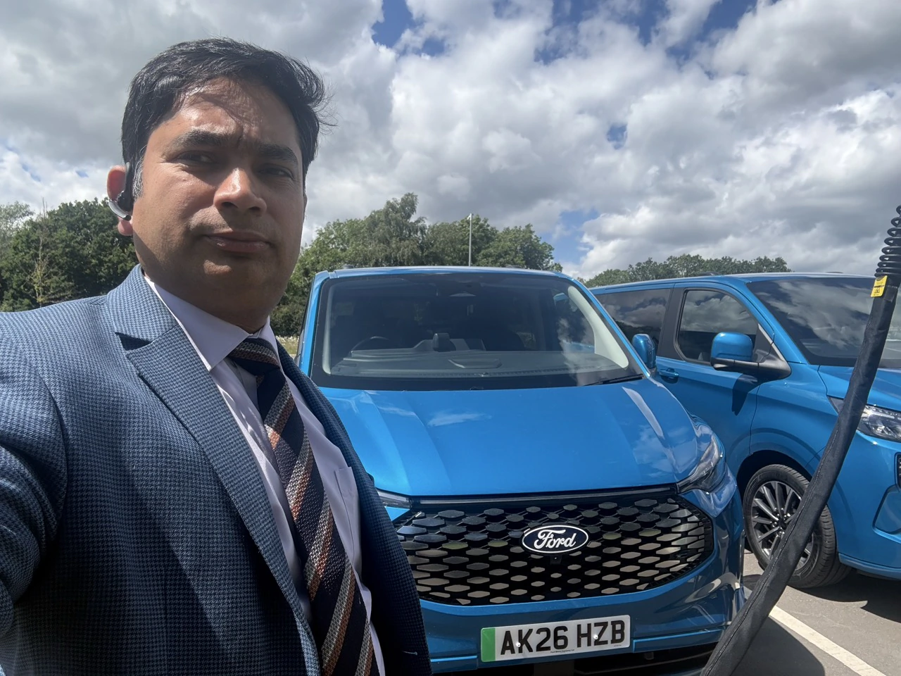 Suited PTG chauffeur beside blue Ford event vehicles in Milton Keynes