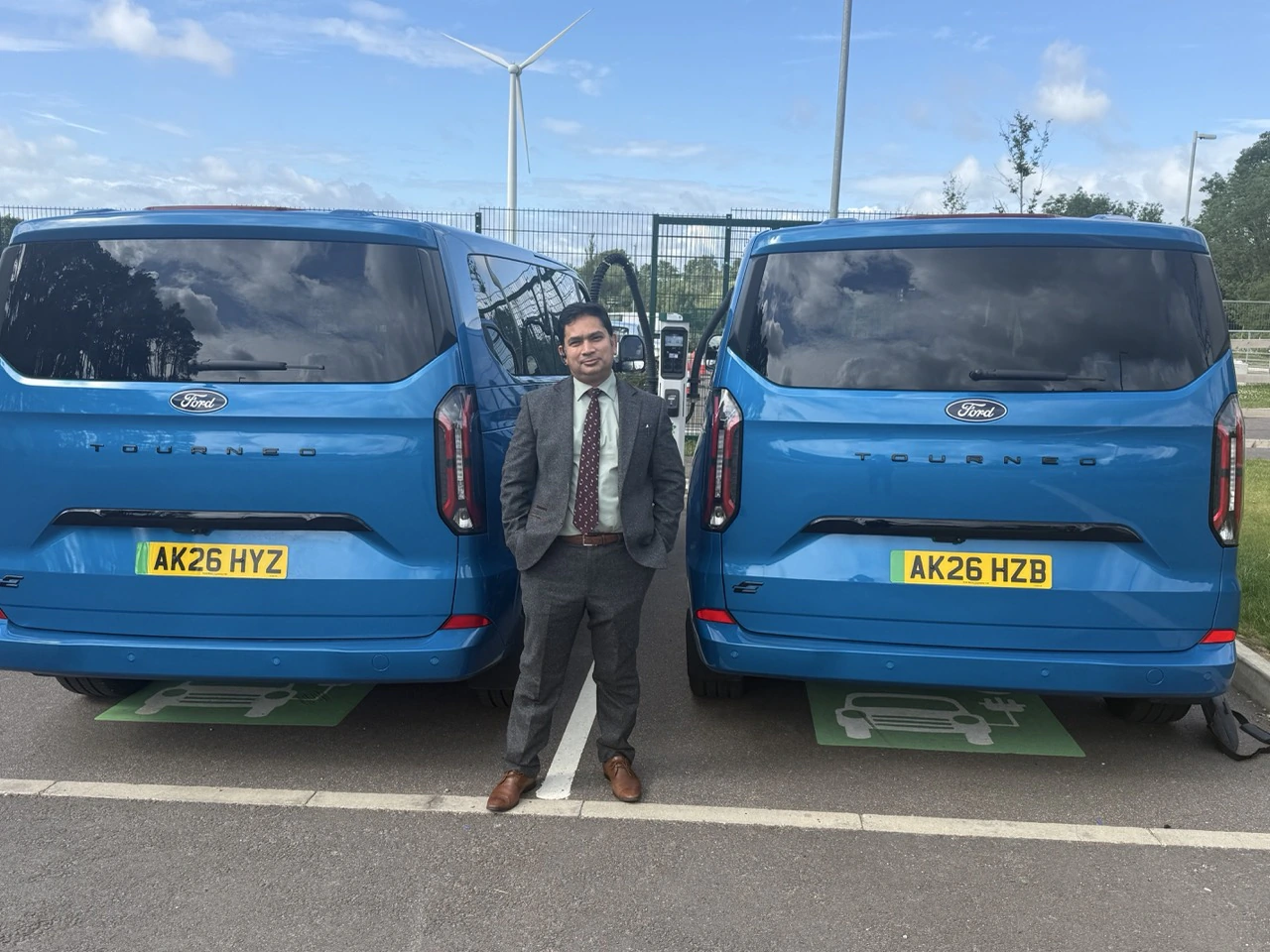 PTG chauffeur standing between two blue Ford Tourneo vehicles at a brand event in Milton Keynes